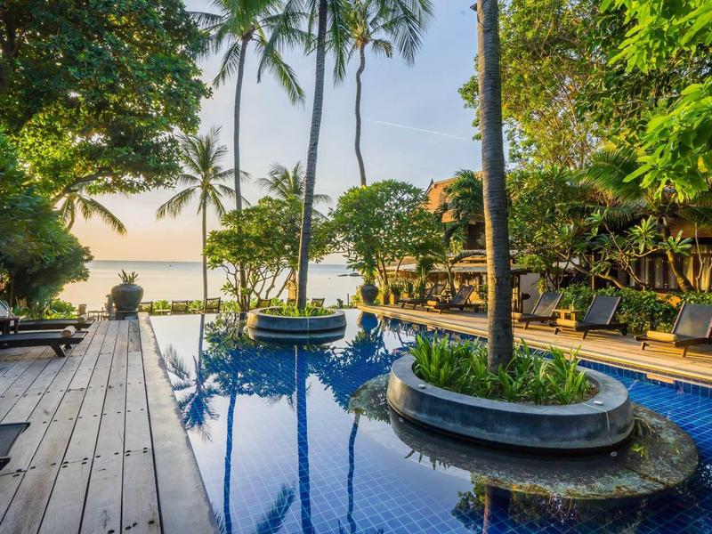 Infinity pool with palm trees and lounge chairs at sunset in a tropical resort.