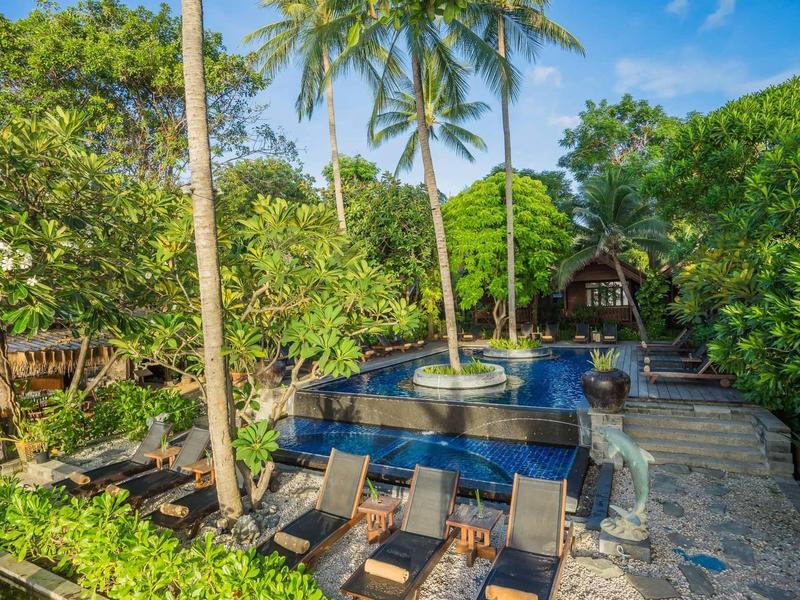 View of garden pool with sun loungers and lush tropical vegetation