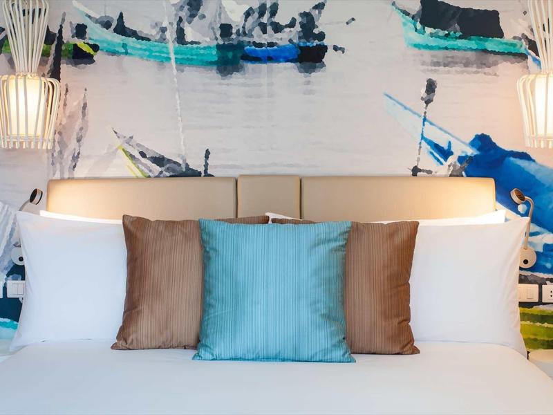 Cozy hotel bed with colorful pillows against a nautical wall decoration featuring boats
