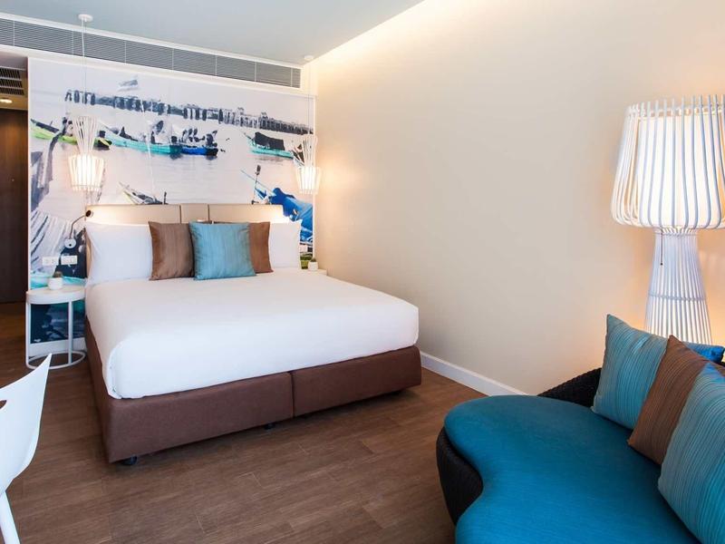 Modern hotel room with double bed, seating area, and wall decoration.