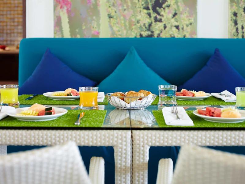 Breakfast table with sandwiches, juices, and water in front of blue sofa with cushions.