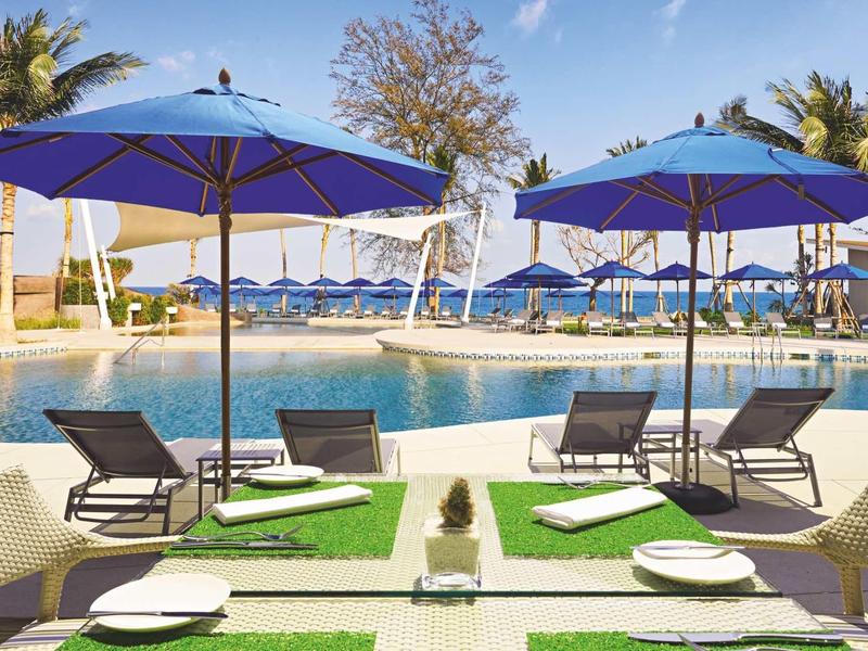 Pool area with lounge chairs, umbrellas, and set tables on a sunny day