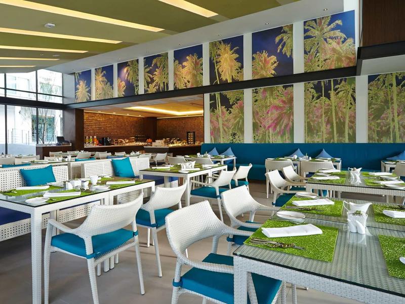 Modern restaurant interior with white tables, colorful chairs, and nature pictures on the wall.