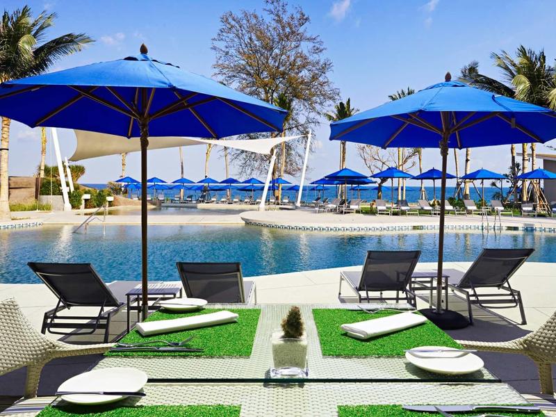 Pool area with blue umbrellas, lounge chairs, and set tables in a hotel resort.