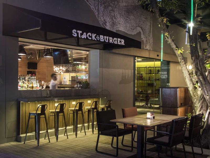 Stylish outdoor restaurant terrace with bar counter and seating under illuminated tree.