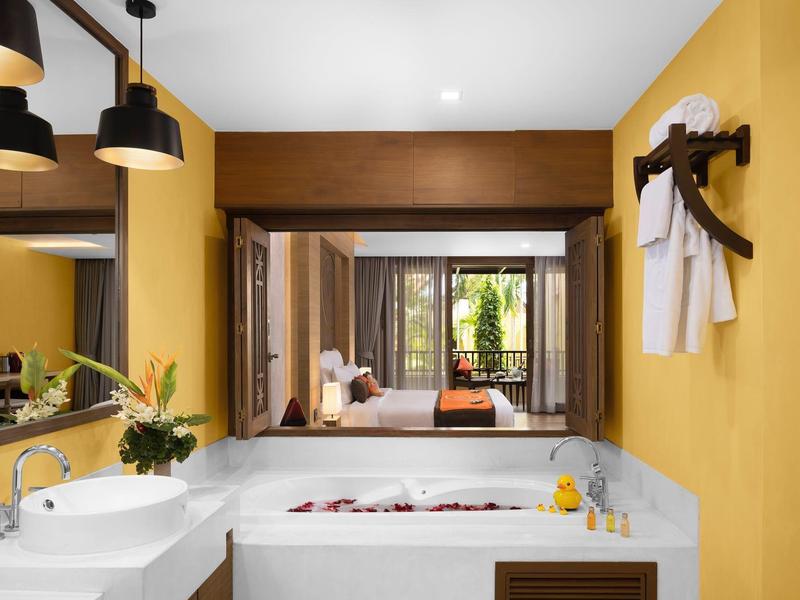 Moderní koupelna s vanou, dvěma umyvadly a teplými žlutými stěnami v hotelovém pokoji.