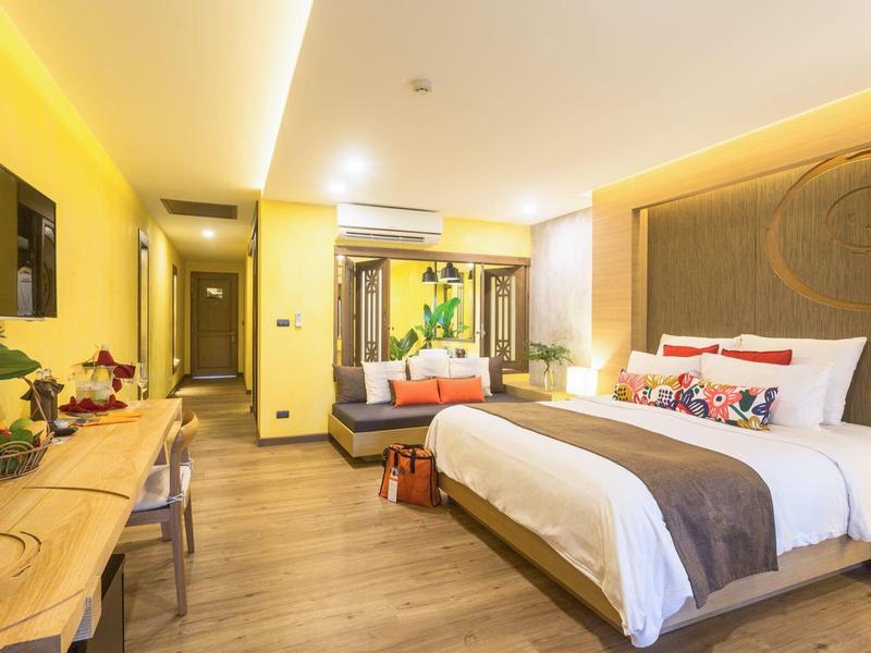 Moderní hotelový pokoj s velkou postelí, pohovkou, stolem a teplým osvětlením.