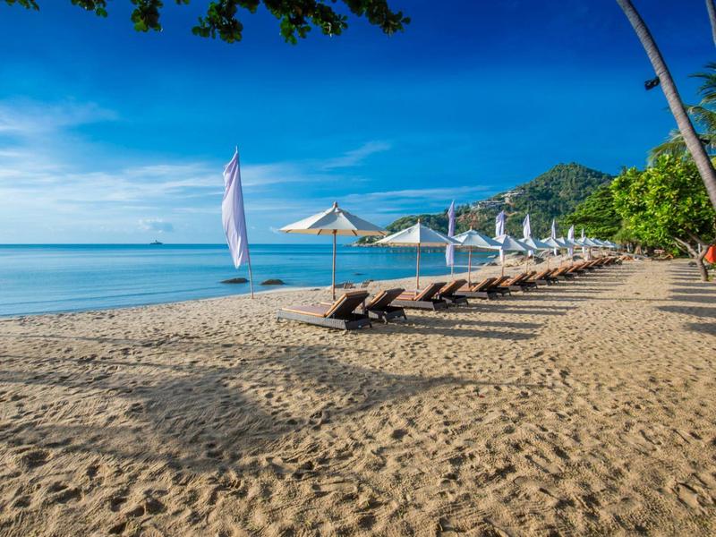 Pláž s lehátky a slunečníky u klidného moře a jasné oblohy.