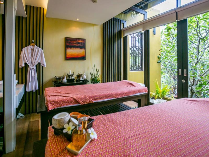 Světlá místnost spa se dvěma masážními lehátky a výhledem na zelené rostliny.