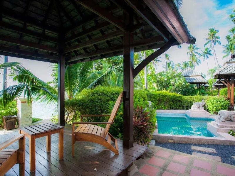 Drewniany zadaszony taras z huśtawkami obok basenu w tropikalnym otoczeniu.