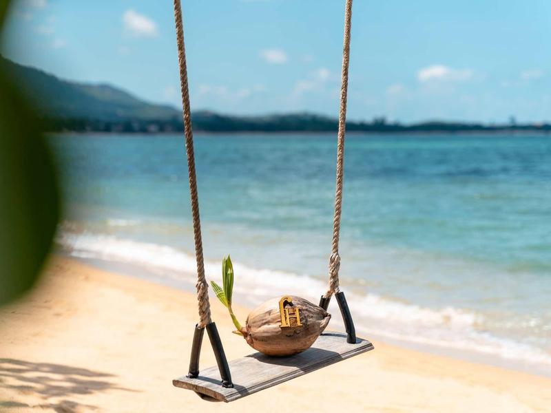 Huśtawka zawieszona na linach z widokiem na piaszczystą plażę i morze.