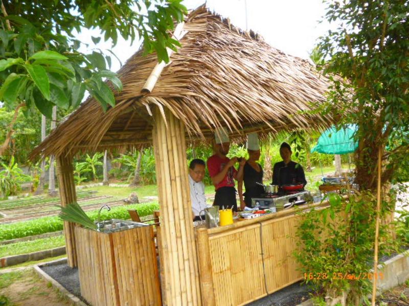 Otwarta chata z bambusa z dachówką z trzciny, ludzie serwują napoje w zielonym otoczeniu.