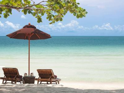 Zwei Liegestühle unter einem Sonnenschirm am ruhigen Strand mit Blick auf das Meer.