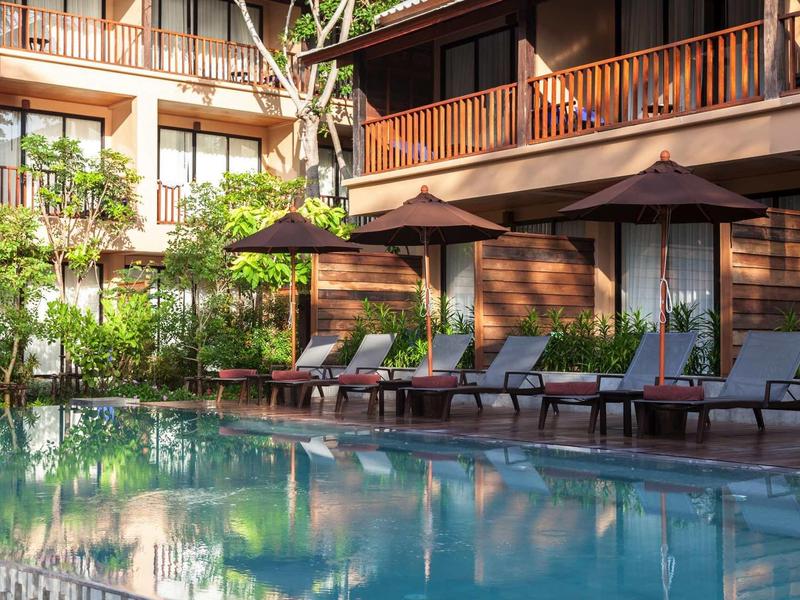 Einladender Pool mit Liegestühlen und Sonnenschirmen vor einem Holzhaus in sonnigem Ambiente.