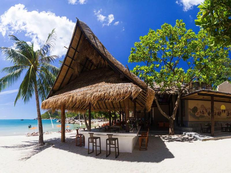 Strandbar mit Strohdach, Palmen und weißem Sandstrand unter blauem Himmel am Meer.