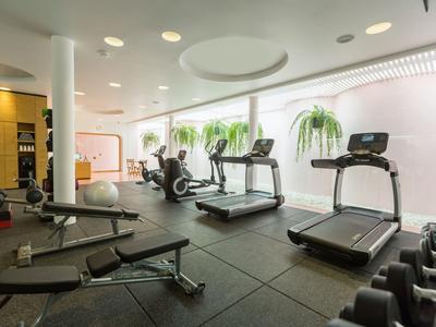 Palestra luminosa con tapis roulant, manubri e pesi accanto a grandi finestre con piante.