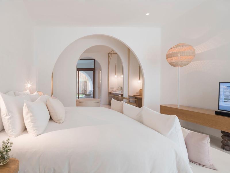 Camera d'hotel minimalista con archi bianchi, letto accogliente e TV moderna.