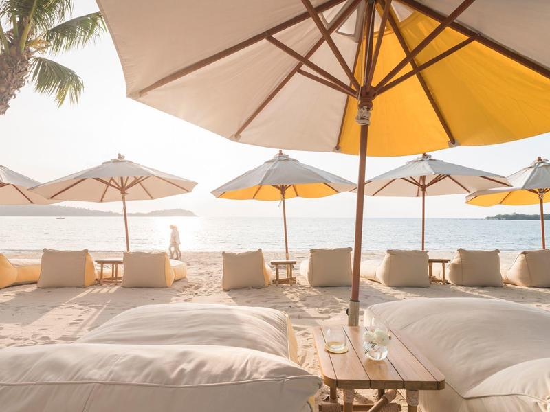 Lettini da spiaggia con cuscini sotto grandi ombrelloni vicino al mare al tramonto.