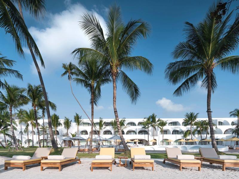 Lettini e palme davanti a un edificio bianco di un hotel sotto un cielo blu