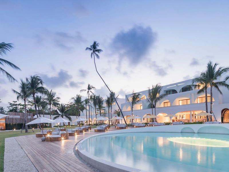Hotel di lusso con piscina illuminata, palme e atmosfera rilassata serale.