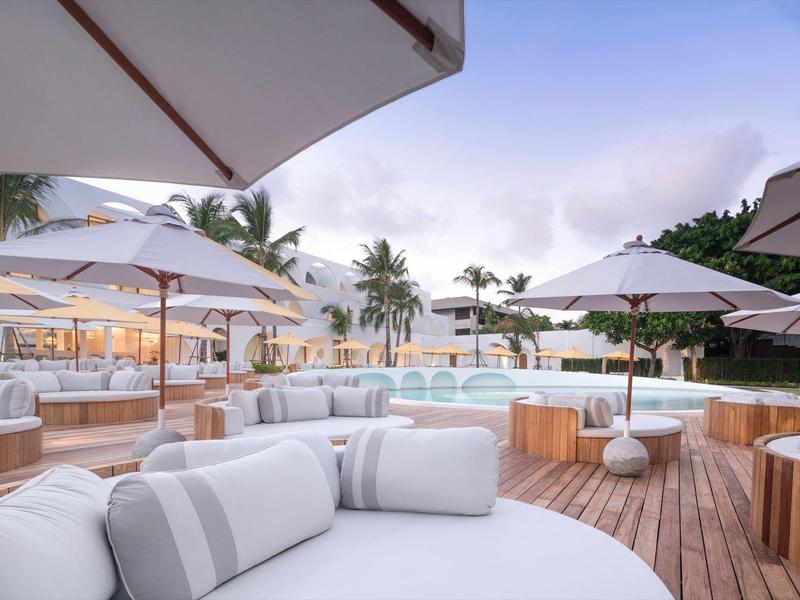 Lounge esterna di lusso con sedute bianche e ombrelloni su un deck in legno al tramonto.