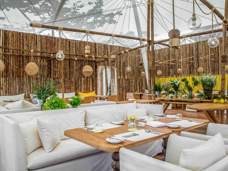 Lounge luminosa con divani bianchi e tavoli in legno in un moderno ristorante all'aperto.