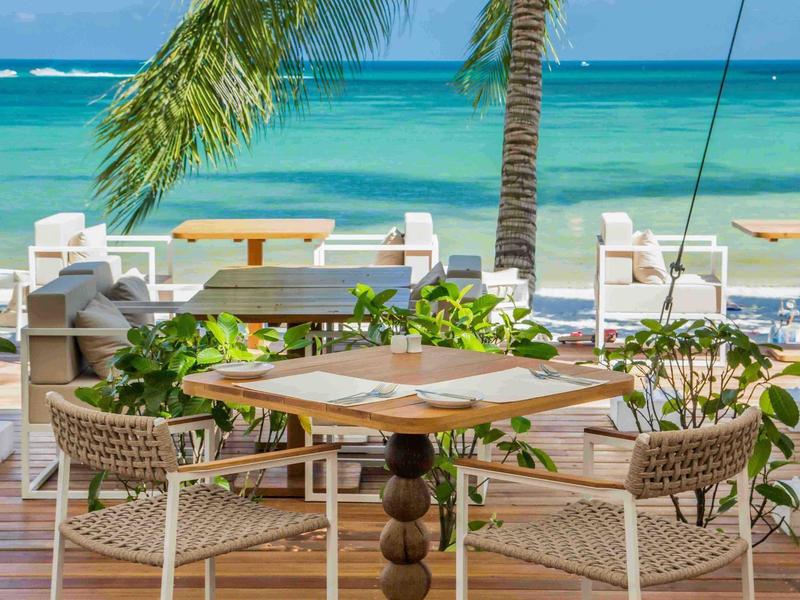 Terrazza del ristorante con tavoli e sedie su una spiaggia tropicale con palme sullo sfondo