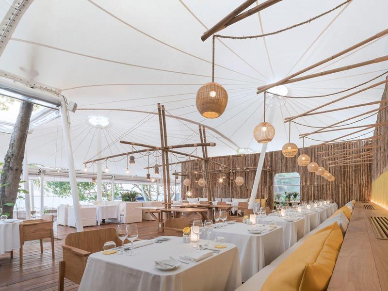 Ristorante moderno e luminoso con tovaglie bianche, elementi in legno e cuscini comodi.