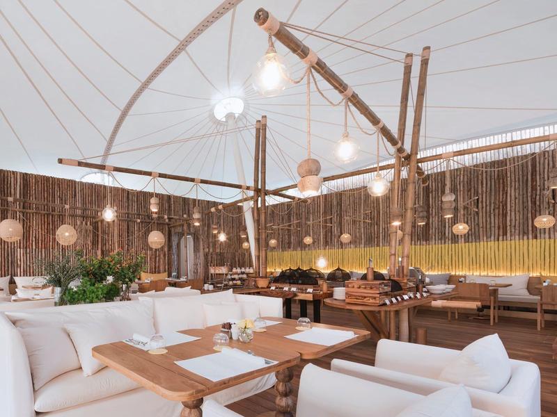 Sala da pranzo moderna con poltrone bianche, tavoli in legno e illuminazione calda.