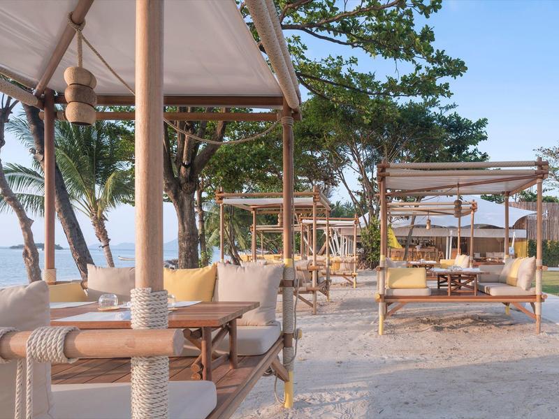 Lettini da spiaggia con tende e cuscini sotto gli alberi su spiaggia sabbiosa con vista mare.