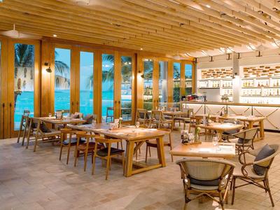 Modernes, helles Restaurant mit Holzmöbeln und Blick auf einen Pool.