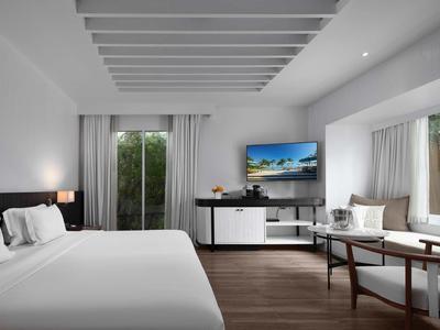 Modernes Hotelzimmer mit großem Bett, Fernseher, Tisch und großen Fenstern mit Vorhängen.