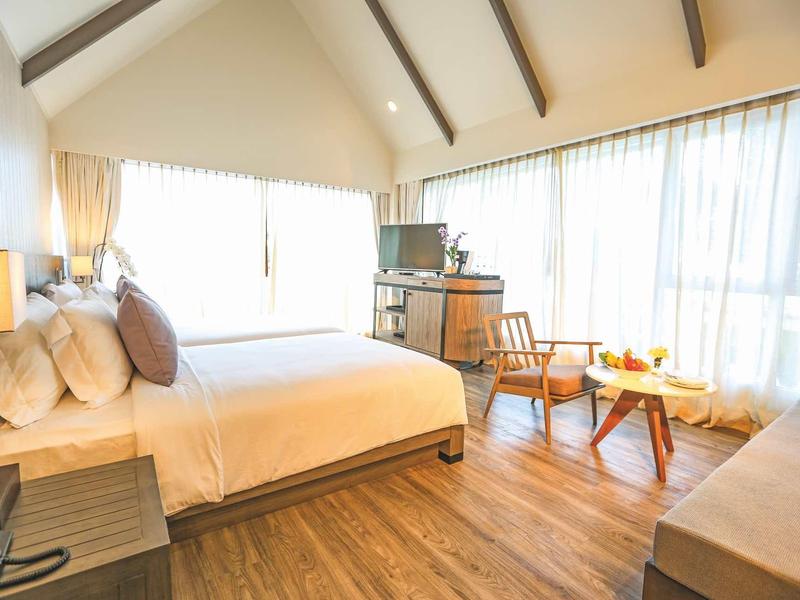 Helles Schlafzimmer mit großem Bett, Holzboden, Stühlen, Tisch und großen Fenstern mit Vorhängen.