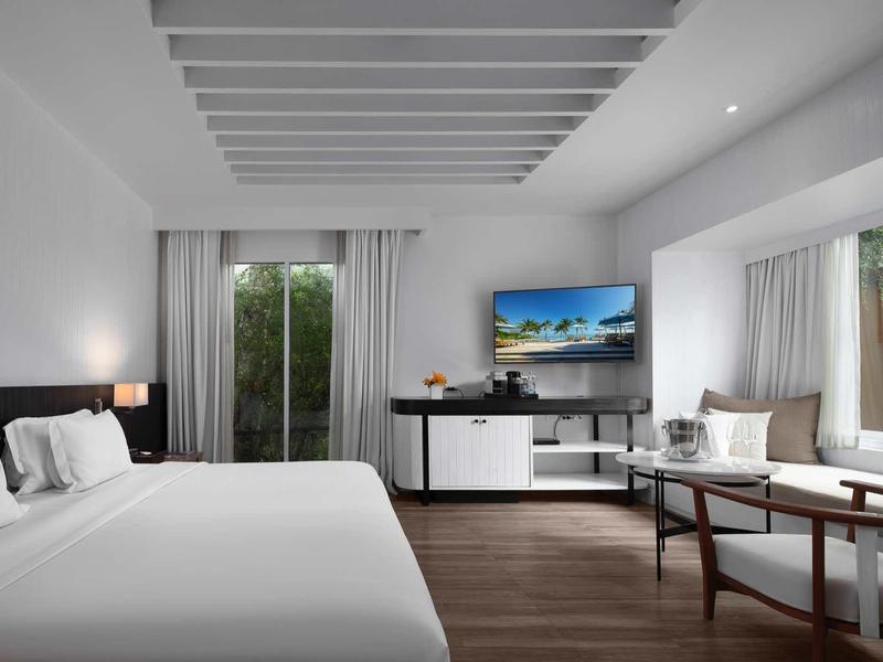 Modernes Hotelzimmer mit großem Bett, Fernseher, Tisch und großen Fenstern mit Vorhängen.