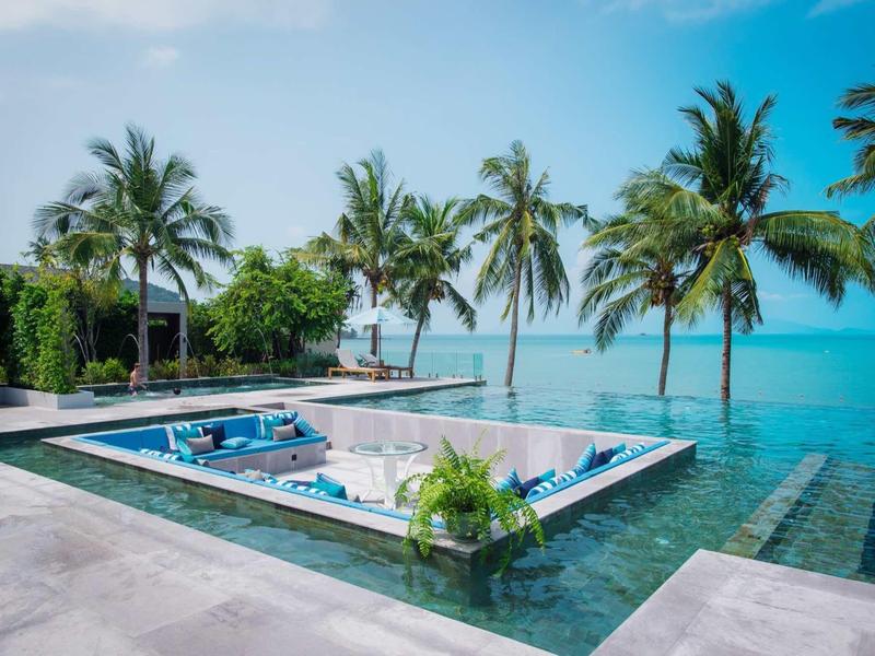 Moderner Pool mit Pflanzen und Palmen am Meer unter blauem Himmel, klar und sonnig.