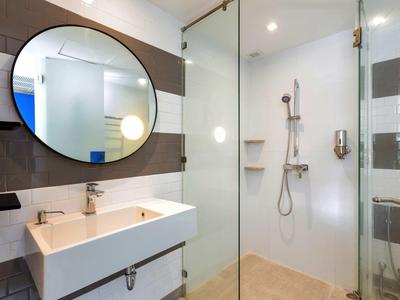 Bagno moderno con grande specchio tondo, lavabo e doccia a filo con parete in vetro.