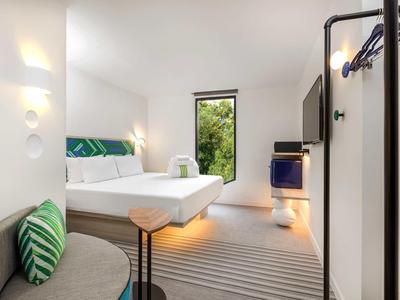 Camera d'hotel moderna con letto, divano e piccolo tavolo in un ambiente luminoso.