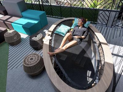 Persona si rilassa su una poltrona ovale con acqua, circondata da sedute moderne su una terrazza.