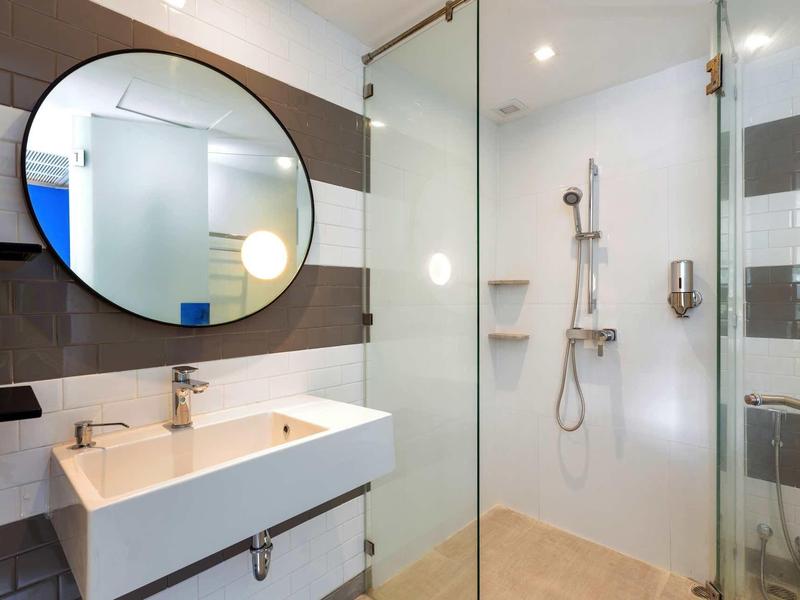 Ducha moderna de hotel con mampara de vidrio, lavabo blanco y espejo redondo.