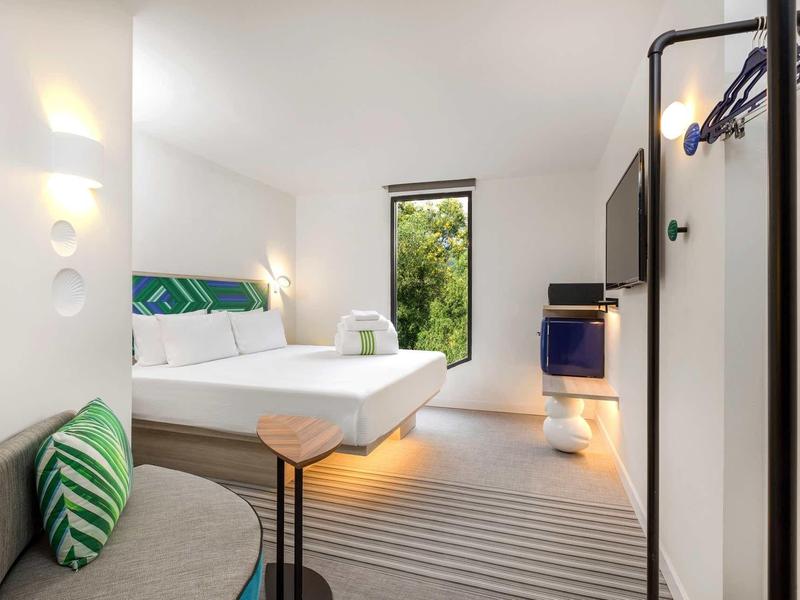 Habitación de hotel moderna con cama grande, sofá gris, alfombra y vista natural por la ventana.