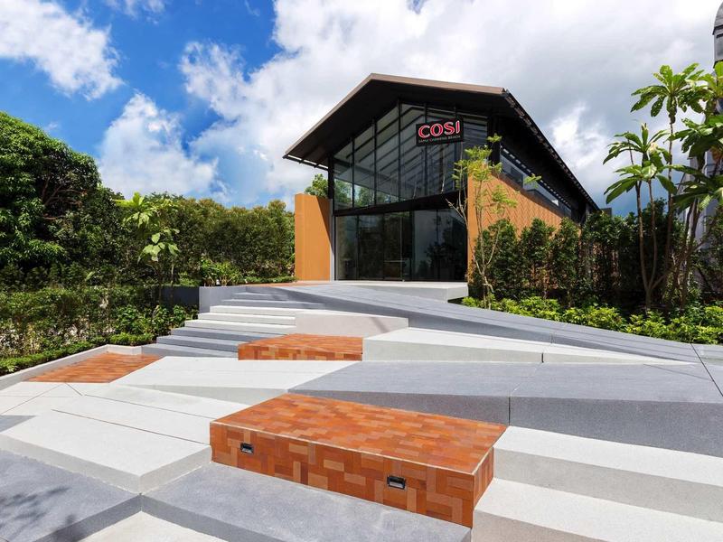 Lodge moderna con fachada de vidrio, rodeada de plantas verdes bajo un cielo azul.