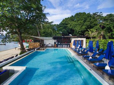 Basen z niebieskimi leżakami i widokiem na plażę przy częściowo pochmurnym niebie