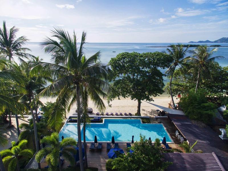 View of a pool surrounded by palm trees on the beach with the sea in the background.