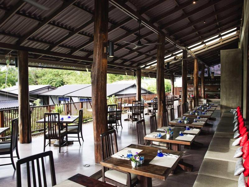 Open restaurant with wooden pillars and elegantly set tables in a natural setting.
