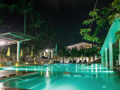 Nachtaufnahme eines beleuchteten Hotelpools mit Palmen und Sitzbereichen.