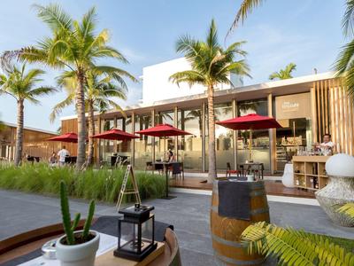 Moderner Außenbereich mit Palmen, Holzmöbeln, roten Sonnenschirmen und dekorativen Pflanzen.