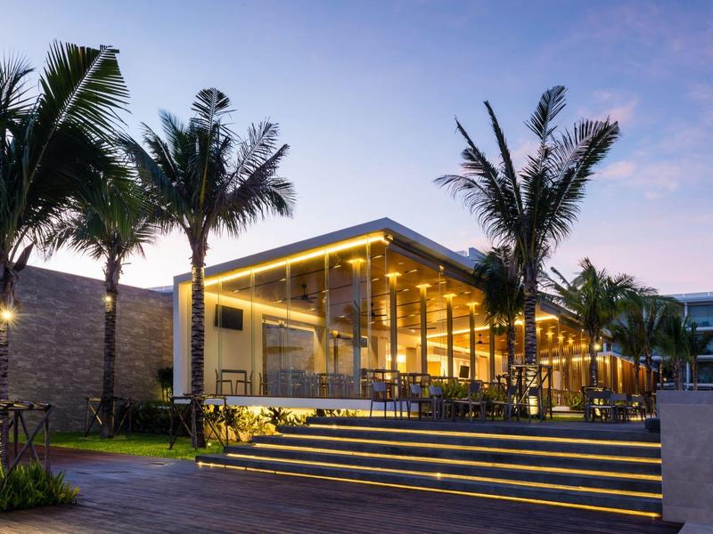 Modernes Hotel mit beleuchteten Treppen und Palmen bei Dämmerung