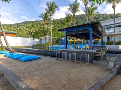 Bar sulla spiaggia moderna con cuscini blu e vista su palme e colline.