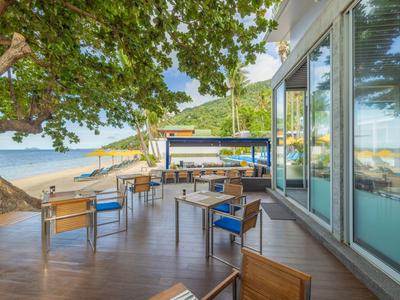 Terrasse mit Tischen und Stühlen, Blick auf Strand und Meer bei Sonnenschein.