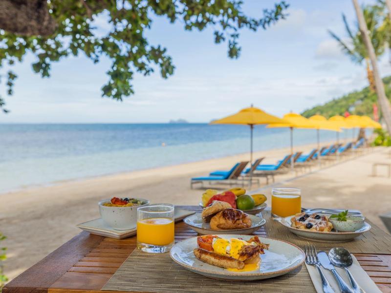 Colazione accogliente sulla spiaggia con vista mare e lettini blu sullo sfondo.
